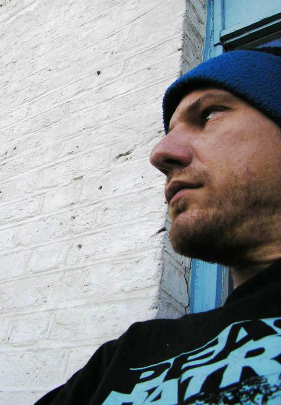 J-Lab Jon Dickens. Facing a white wall. Underground look. Blue cap on head and trendy t-shirt with print